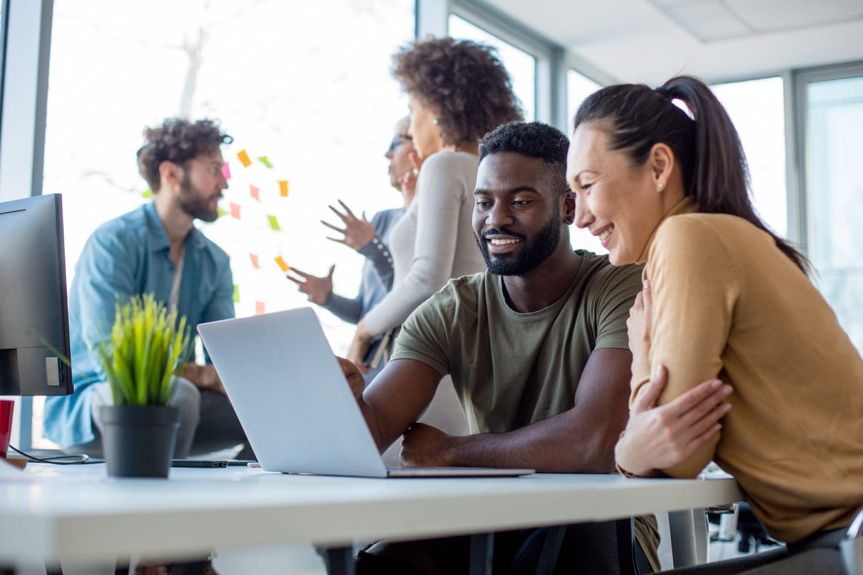 A man and woman work at a laptop, while others chat behind them in the window. Our inventory management system is here to help you reach your goals