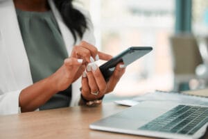 A woman types on a phone with a laptop in front of her. The Valley list can help with mobile-first web design.