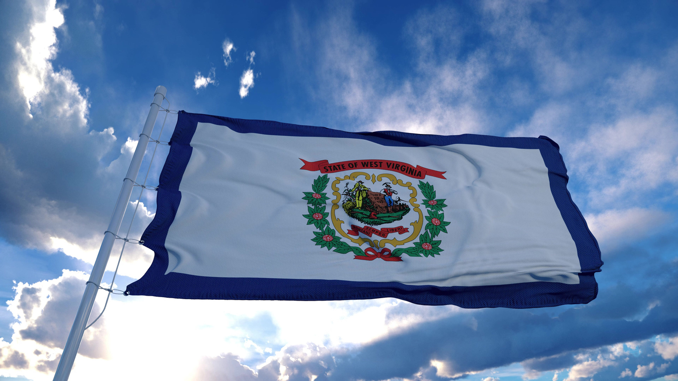 West Virginia flag on a flagpole waving in the wind, blue sky background. The Valley List is here to be your white label support in Huntington.