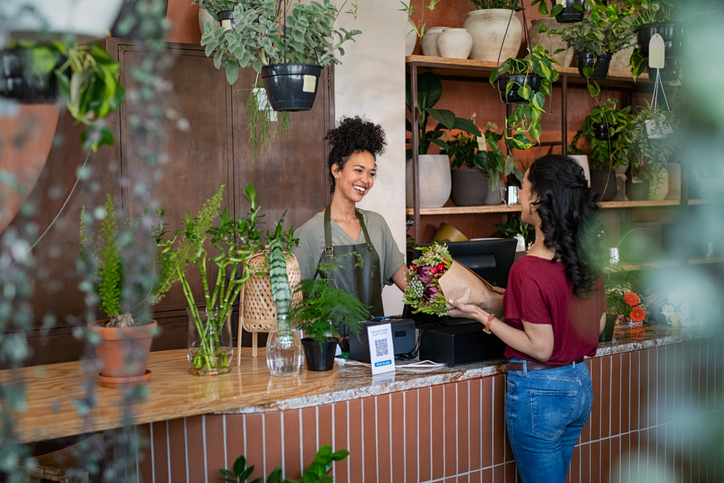 A smiling woman works in a plant shop, speaking with a customer. The Valley List is proud to offer website hosting in Bexley, Ohio.