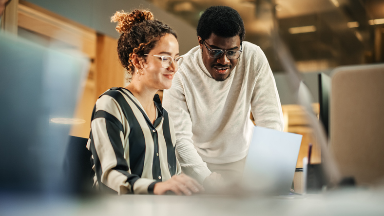 A man and a woman sit at a desk in a business setting and look at a laptop together. Web Impact Marketing and The Valley List have joined together to be a reliable SEO services in Westerville, Ohio.