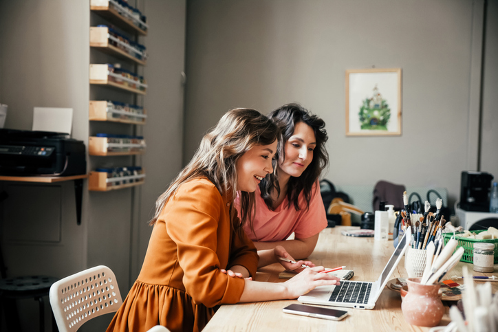Two young women work on a computer. Web application development is essential to growing your business.