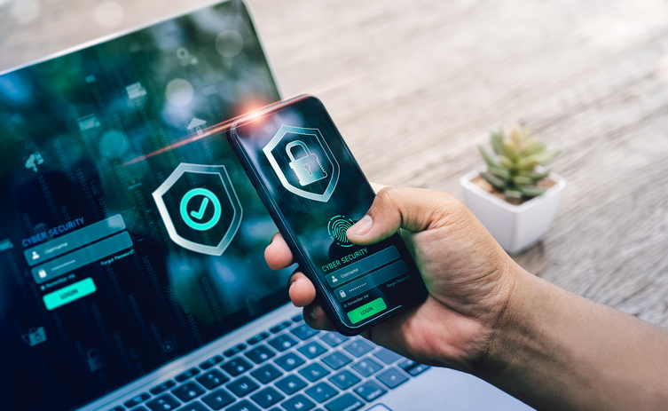 A photo of a person's hand with a laptop and a phone, passing a security checking. The Valley List provides managed web hosting with a high level of digital security.