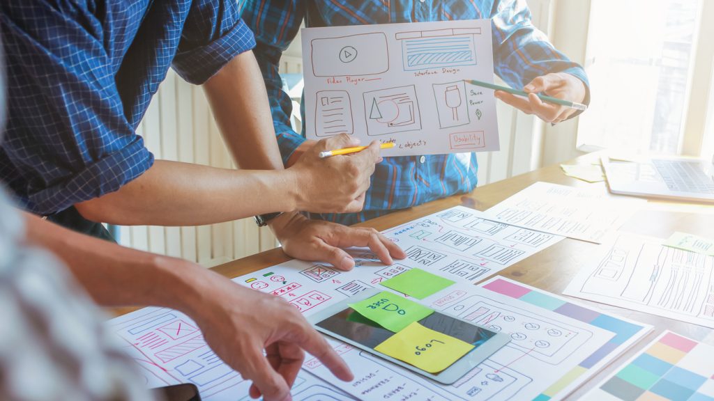 A group of people create a website using paper notes and drawings. Only their hands are visible.