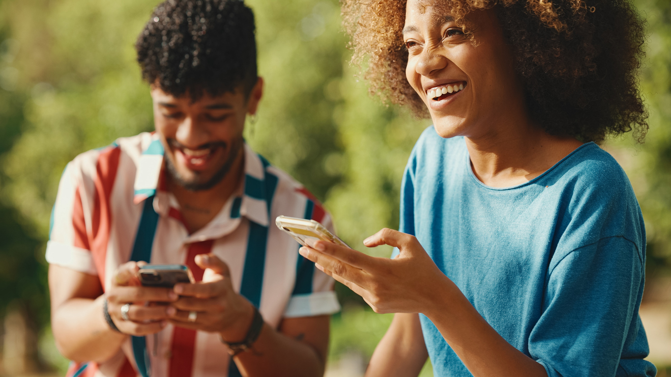 Close-up of young smiling woman with curly hair wearing blue t-shirt sitting in park along with her friend. The Valley List offers user friendly mobile app design and app development in Seguin, Texas.
