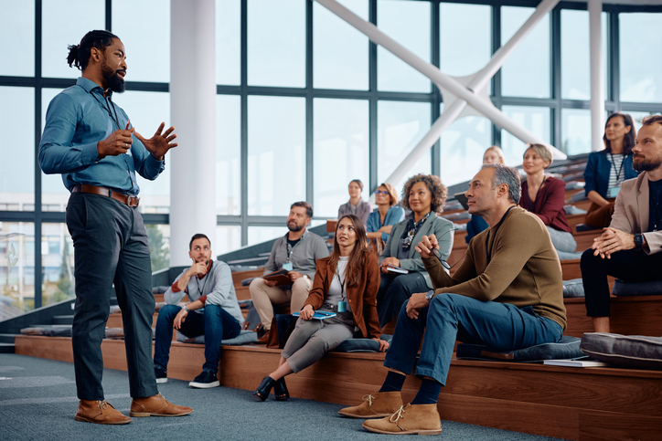 A speaker stands in front of a group of people, speaking to them. As a website design company, we prioritize building your brand and your business with mobile design, local knowledge, and excellent website design.