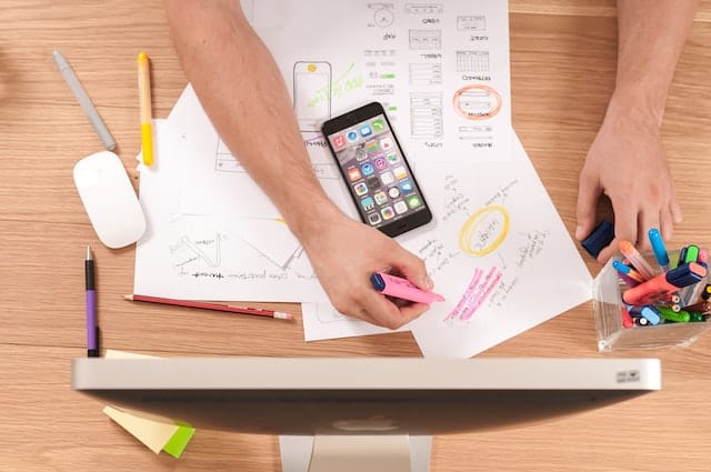 Man drawing a website wireframe and taking notes with smartphone on desk