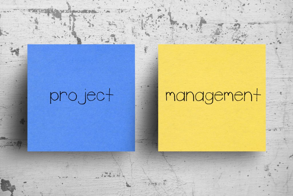 Two blue and yellow sticky notes on a concrete wall that say project management. The benefits of project management can effect your personal life.